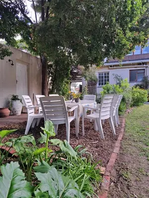 a group of white chairs and a table in a yard at Home On Uitvlugt - Peaceful leafy garden flat with sunny lounge in Cape Town