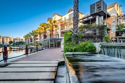 a walkway in front of a building with palm trees at Quayside Canal Eden Home in Cape Town