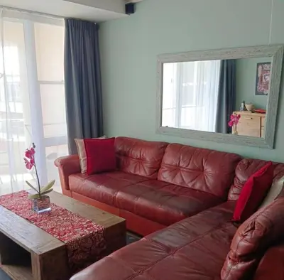 a living room with a red leather couch and a mirror at Lagoon Beach Apartment 309 in Cape Town