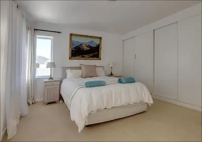 a white bedroom with a bed and a window at Seaclusion in Hermanus