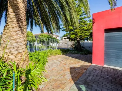 a palm tree next to a red building with a garage at Two Palm House - Vermont Hermanus in Hermanus