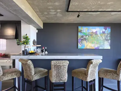 a kitchen with a bar with chairs and a painting on the wall at iMoyo Ocean Villa and Studio, Hermanus in Hermanus