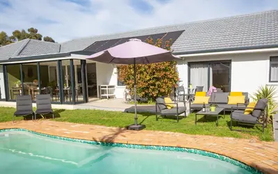 a patio with chairs and an umbrella next to a pool at Casa iLanga guesthouse in Somerset West