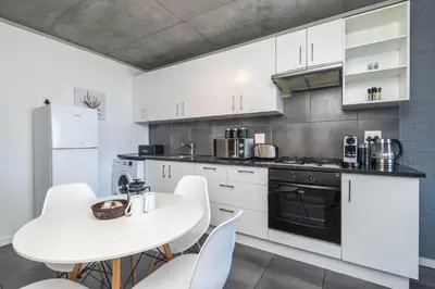 a kitchen with white cabinets and a white table and chairs at 2 Bedroom Secure Pool Strong WiFi in Cape Town