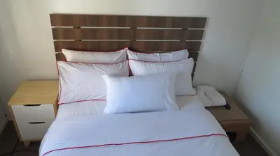 a bed with white pillows and a wooden headboard at Galaxy Sleep And Go Rooms Goodwood in Cape Town