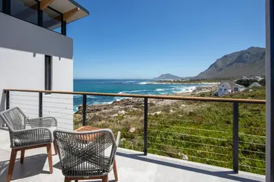 a balcony with two chairs and a view of the ocean at OnTheRocksBB Solar Powered Guesthouse and Ocean Lodge in Bettyʼs Bay