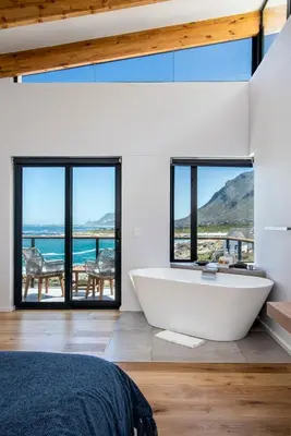 a bath tub in a bedroom with a view of the ocean at OnTheRocksBB Solar Powered Guesthouse and Ocean Lodge in Bettyʼs Bay