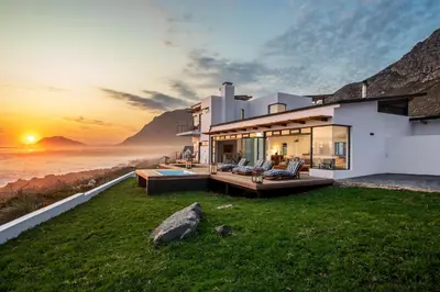 a house with a view of the ocean at sunset at OnTheRocksBB Solar Powered Guesthouse and Ocean Lodge in Bettyʼs Bay
