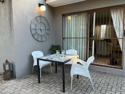 a table and chairs on a patio with a clock at THE CORNER COTTAGE in Somerset West