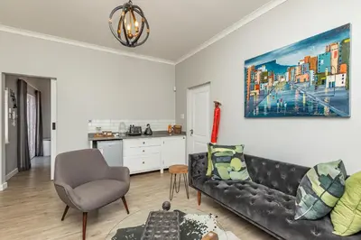 a living room with a black couch and a kitchen at Spacious Guest Apartment in Rondebosch in Cape Town