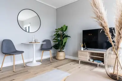 a living room with a tv and two chairs and a mirror at Burmeister403 - Modern 1 Bedroom Apartment across from Ocean in Cape Town