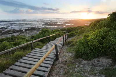 a wooden staircase leading to the ocean at sunset at TnT on Main in Hermanus