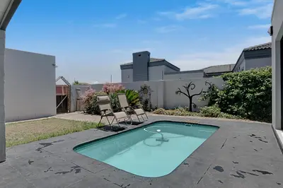 a swimming pool with two chairs in a yard at Spacious Shared 3-Bedroom Villa Near Blouberg Beach Pool, Wi-Fi, Braai in Cape Town