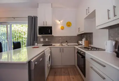 a kitchen with white cabinets and a counter top at Garden- Pool flat with Solar Electricity in Somerset West