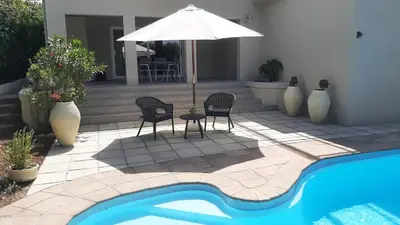 a patio with two chairs and an umbrella next to a pool at Garden- Pool flat with Solar Electricity in Somerset West