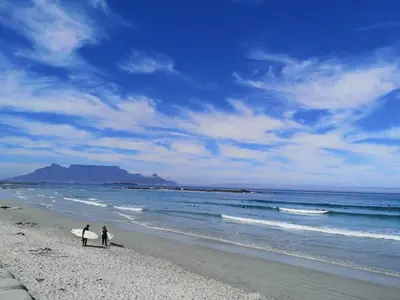 two people walking on the beach with their surfboards at Blouberg Beach Luxury Apartment in Cape Town
