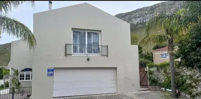 a white house with a garage and a palm tree at Bing Heights Suite in Hermanus
