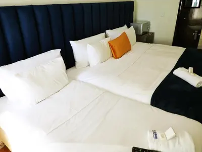 a large bed with white sheets and an orange pillow at El-Gibor Best Guest House in Cape Town