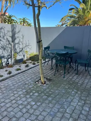 a patio with a table and chairs and a tree at Cowrie Cottage Self Catering in Cape Town