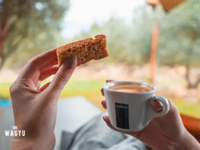 a person holding a piece of food and a cup of coffee at Wagyu Mountain Lodge in Paarl