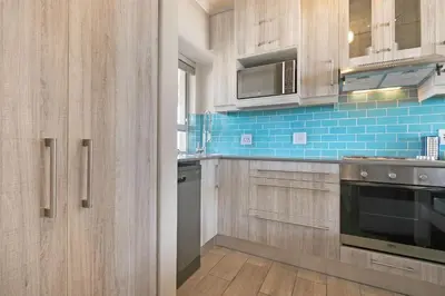 a kitchen with wooden cabinets and blue tiles at Sea Spray B404 in Cape Town