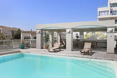 a swimming pool with two chairs and a patio at Sea Spray B404 in Cape Town