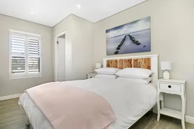 a white bedroom with a large bed and a window at On the Greens Villa in Cape Town