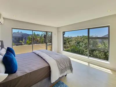 a bedroom with a large bed and large windows at Kite, Wind, Waves Beach Villa in Cape Town