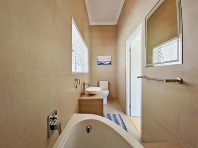 a bathroom with a tub and a toilet and a sink at Kite, Wind, Waves Beach Villa in Cape Town