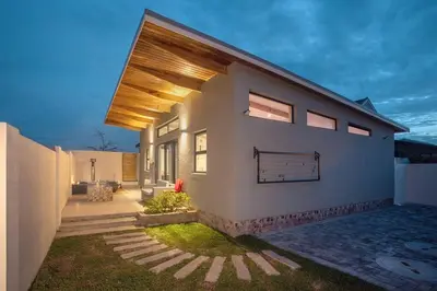a white house with a wooden roof and a yard at Mountain and Sea Cottage in Hermanus
