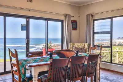 a dining room with a table and chairs and the ocean at Jock's View in Bettyʼs Bay