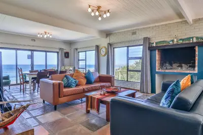 a living room with couches and a fireplace and a table at Jock's View in Bettyʼs Bay
