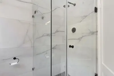 a shower with white marble walls and a glass door at Atlantic Sky Villa in Gordonʼs Bay
