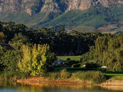 a train on tracks next to a river with mountains at Dawn Mountains Farm in Simondium