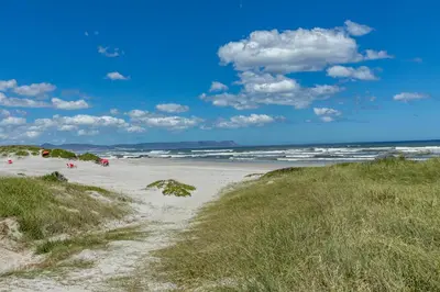 a sandy beach with the ocean in the background at SAM's - Sea And Mountain in Hermanus