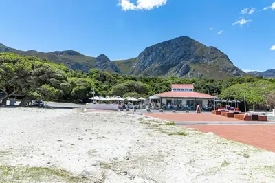 a beach in front of a building with mountains in the background at SAM's - Sea And Mountain in Hermanus