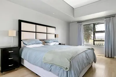 a white bedroom with a large bed and a window at On 8th Green Worthing Villa in Cape Town