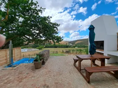a patio with a wooden table and a umbrella at Ou Meul Farm Cottage in Botrivier