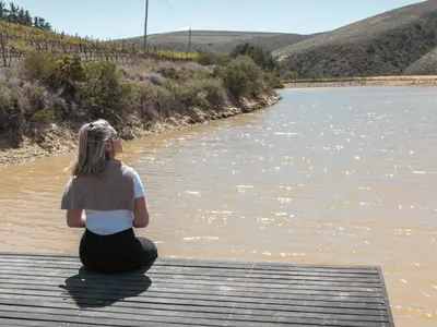 a woman sitting on a dock looking at a river at Ou Meul Farm Cottage in Botrivier