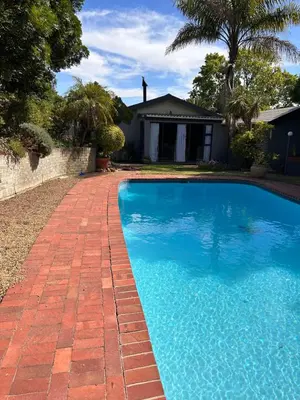 a swimming pool with a brick walkway next to a house at Garden View Inn in Cape Town