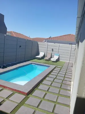 a swimming pool in a backyard with two lawn chairs at Naliya Guest house in Cape Town