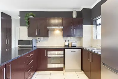 a kitchen with dark wood cabinets and a sink at Waterstone East C103 by Host Agents in Cape Town
