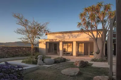 a house with trees and rocks in a yard at Benguela Cove - Oceans Away in Hermanus