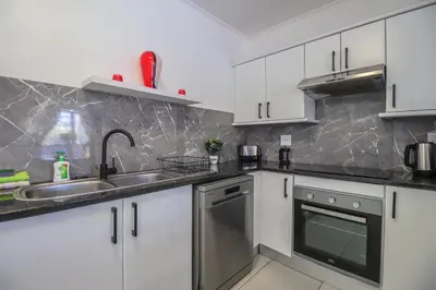 a kitchen with white cabinets and a sink and a dishwasher at 102 Palma Eyrie Holiday Apartments in Cape Town