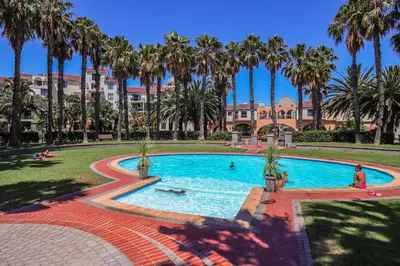 a pool with palm trees and people swimming in it at 102 Palma Eyrie Holiday Apartments in Cape Town
