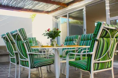 a table with green chairs on a patio at 7th Wonder Beach Guest House in Cape Town
