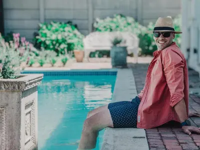 a man in a hat sitting next to a swimming pool at Kolonie's Tuin in Stellenbosch