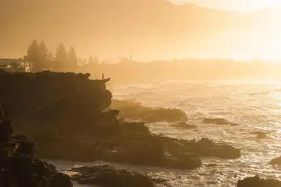 a person standing on a rock near the ocean at Tuis en Tevrede - 1 Bedroom Flat in Hermanus