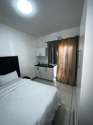 a bedroom with a white bed and a kitchen at Beatrice Guesthouse in Cape Town