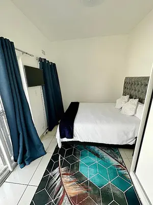 a bedroom with a bed with blue curtains and a rug at Beatrice Guesthouse in Cape Town